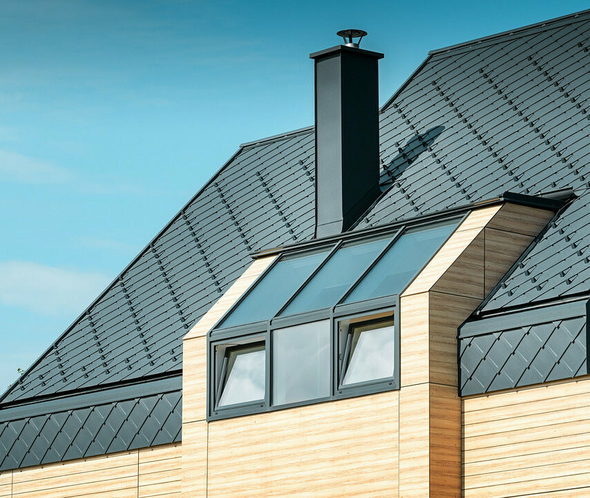Moderne tagudformning med PREFA tagrombe 29 × 29 i P.10 antracit Enfamilieshus med sadeltag uden udhæng med en facade i træ-look og aluminiumstag i antracit