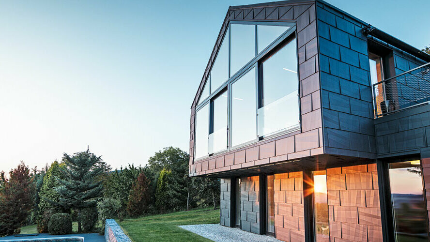 Moderne parcelhus uden tagudhæng med store vinduer og FX.12-facade i antracit, fotograferet ved solnedgang.