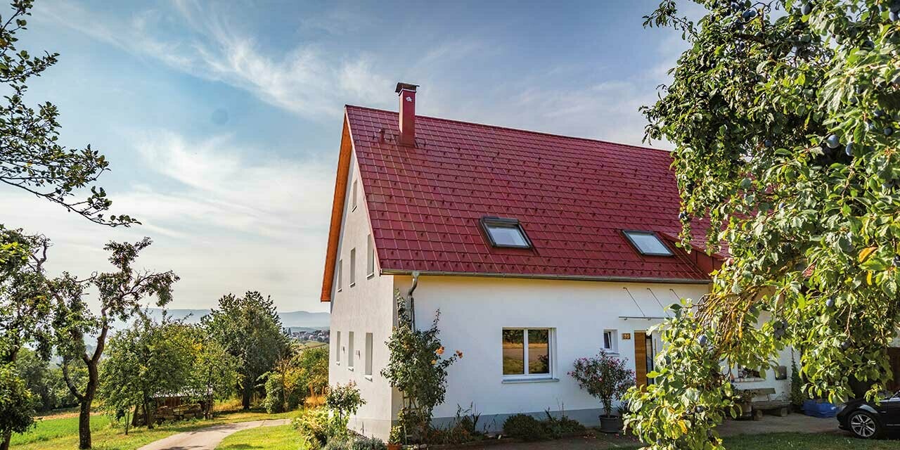 Romantisk lille hus på landet med mange træer og buske. Belagt med et PREFA-tag i oxidrød.