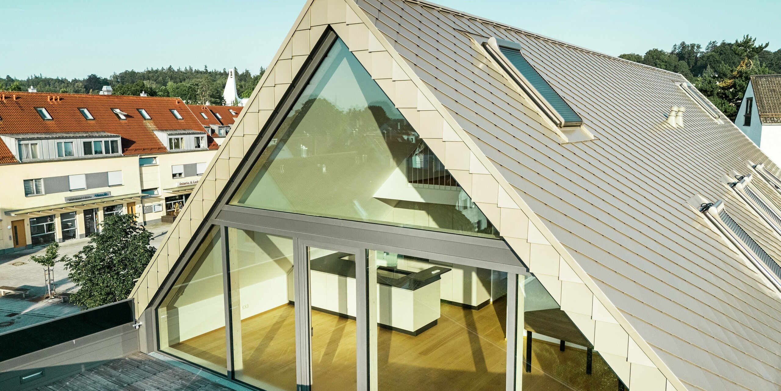 Dachgeschoss eines modernen Mehrfamilienhauses in Leitershofen, Deutschland, mit großzügiger Fensterfront und Balkon. Die Dach- und Fassadenbekleidung besteht aus PREFA Aluminiumrauten in der Farbe Bronze. Die robusten Rauten verleihen dem Gebäude ein elegantes und langlebiges Erscheinungsbild. Das architektonisch anspruchsvolle Design kombiniert klare Linien und großzügige Glasflächen, die für helle und offene Wohnräume sorgen. 