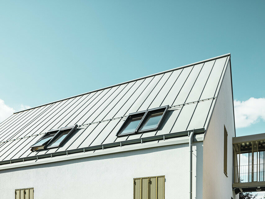 seitliche Ansicht des Wohnhauses eingedeckt mit Prefalz in der Farbe P.10 Zinkgrau bei Sonnenschein