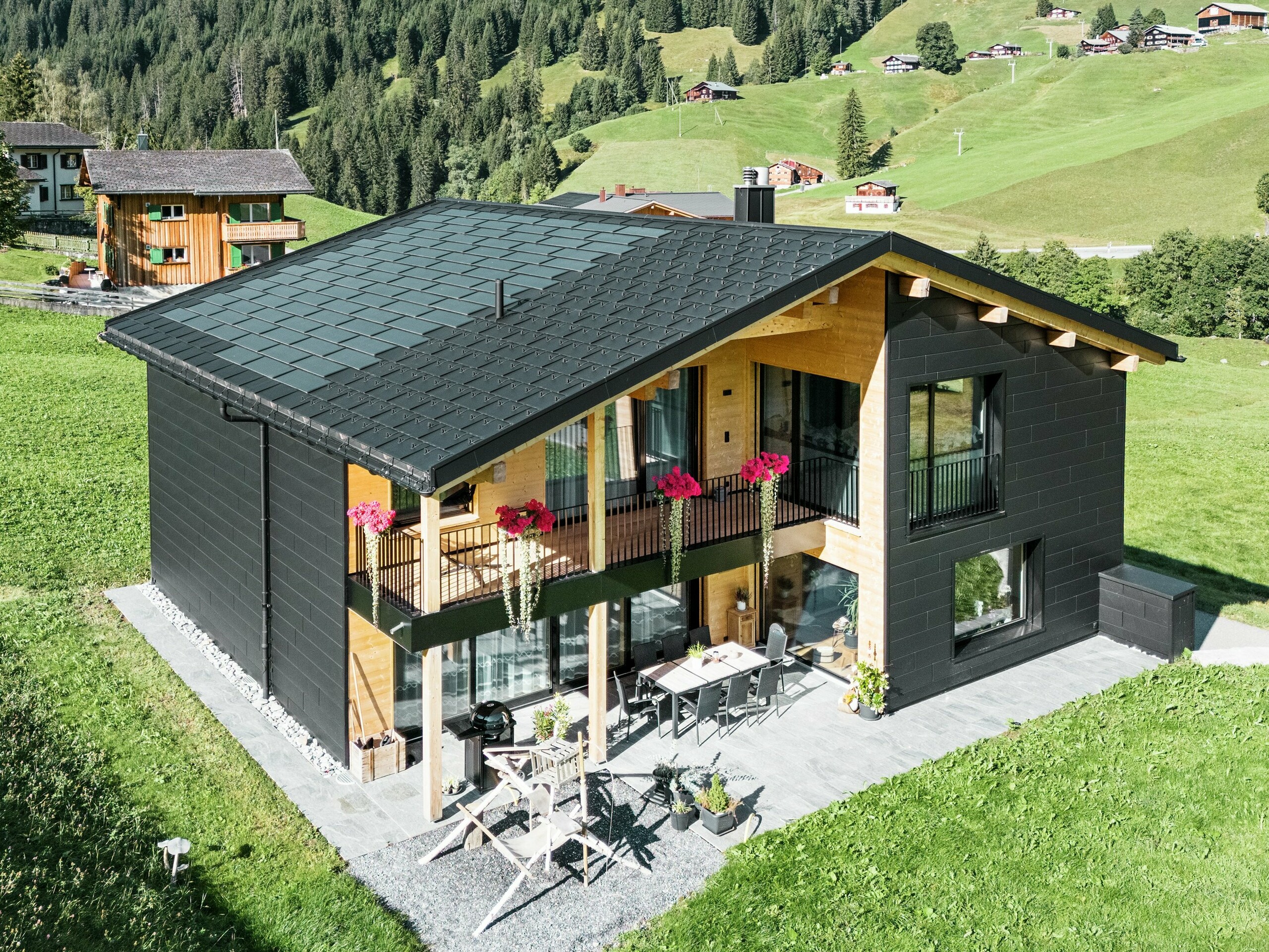 Det elegante parcelhus i de bakkede omgivelser i Ascharina (Schweiz) viser, hvordan aluminium og træ kan kombineres perfekt. De robuste PREFA Siding.X-facadepaneler i P.10 sort harmonerer med taget, der består af PREFA solcelletagpaneler og R.16-tagpaneler i samme farve. Den holdbare aluminiumsbeklædning beskytter bygningen pålideligt mod udfordringerne i det alpine klima.