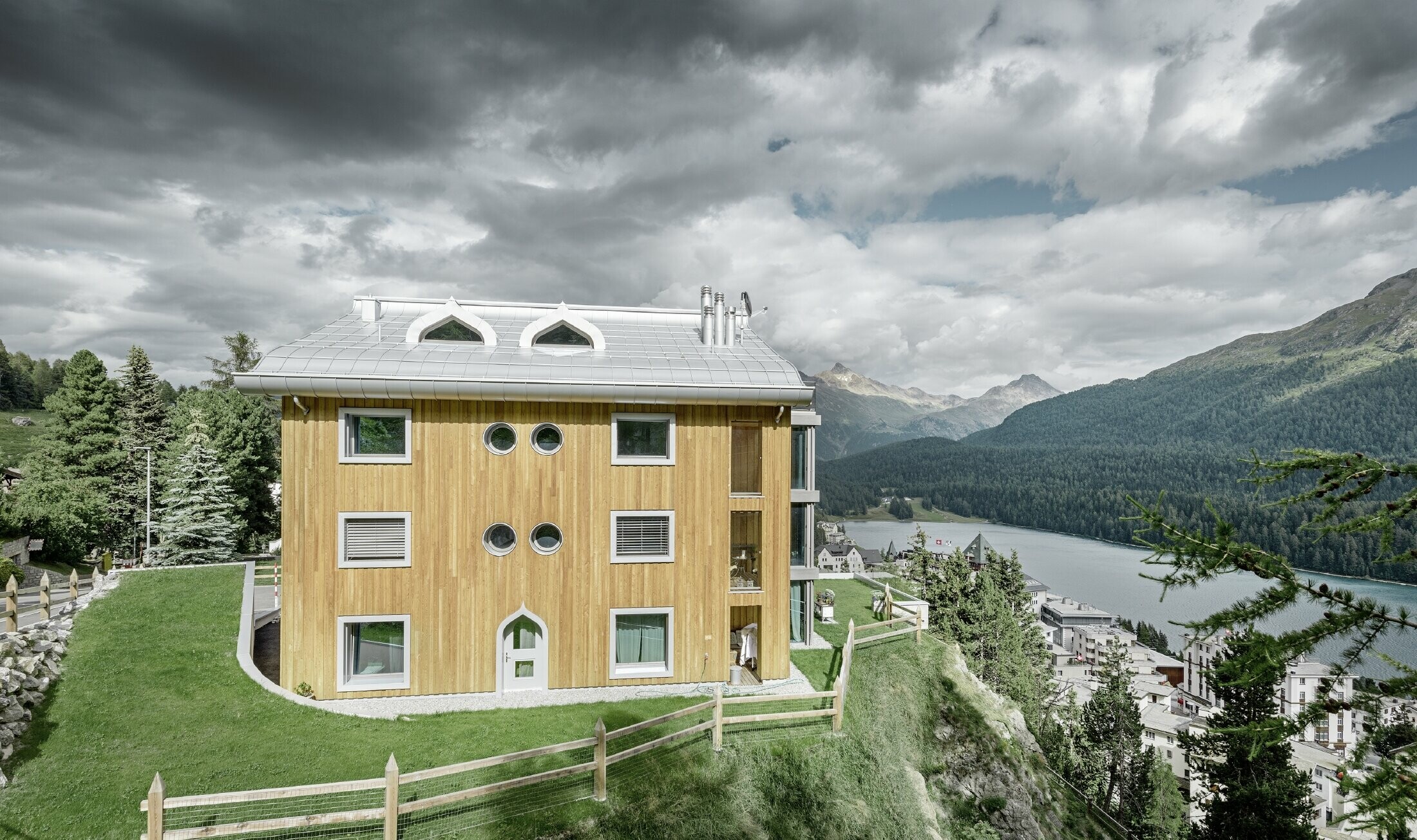 Boliganlæg i St. Moritz med træfacade og aluminiumtag med svunget tagrende i sølvmetallic