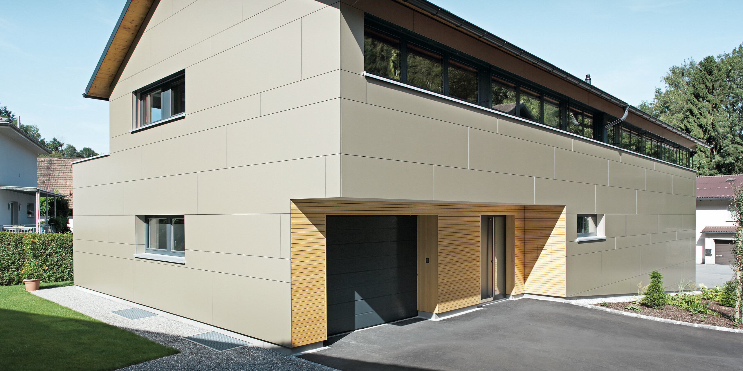 Elegantes Einfamilienhaus in Hohenems, ausgestattet mit einem PREFA Komplettsystem. Die Fassade besteht aus Aluminium Verbundplatten in Bronzemetallic, die einen modernen und klaren Look schaffen, während die Holzelemente am Garageneingang Wärme und Natürlichkeit ausstrahlen. Das Dach ist mit PREFA Dachplatten in P.10 Anthrazit gedeckt, die zusammen mit der Fassade ein architektonisches Gesamtkonzept bilden und das Haus effektiv schützen.