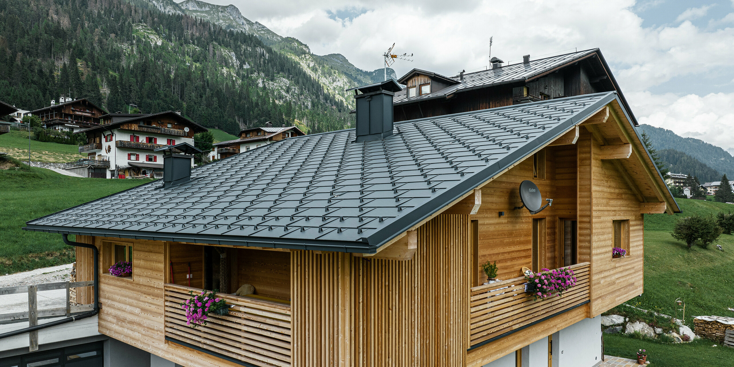 Seitenansicht eines Einfamilienhauses in Sappada, Italien, mit einem perfekt integrierten PREFA Dachsystem aus Dachplatten R.16 in P.10 Schwarz. Das Dach fügt sich harmonisch in die traditionelle Holzfassade und die alpine Landschaft ein. Die Kombination aus modernen, robusten Aluminiumdachplatten und natürlicher Holzarchitektur spiegelt die ökologische Bauweise und die Anpassung an die Region wider, was die Casa Hoffe zu einem Paradebeispiel für nachhaltiges Bauen in den Alpen macht.