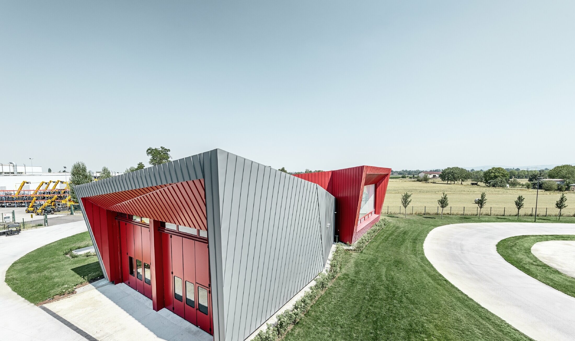 Moderne træningscenter fra Dieci i Montecchio Emilia , Italien, med tribune med aluminiumfacade med Prefalz i lysegrå og Falzonal i karminrød