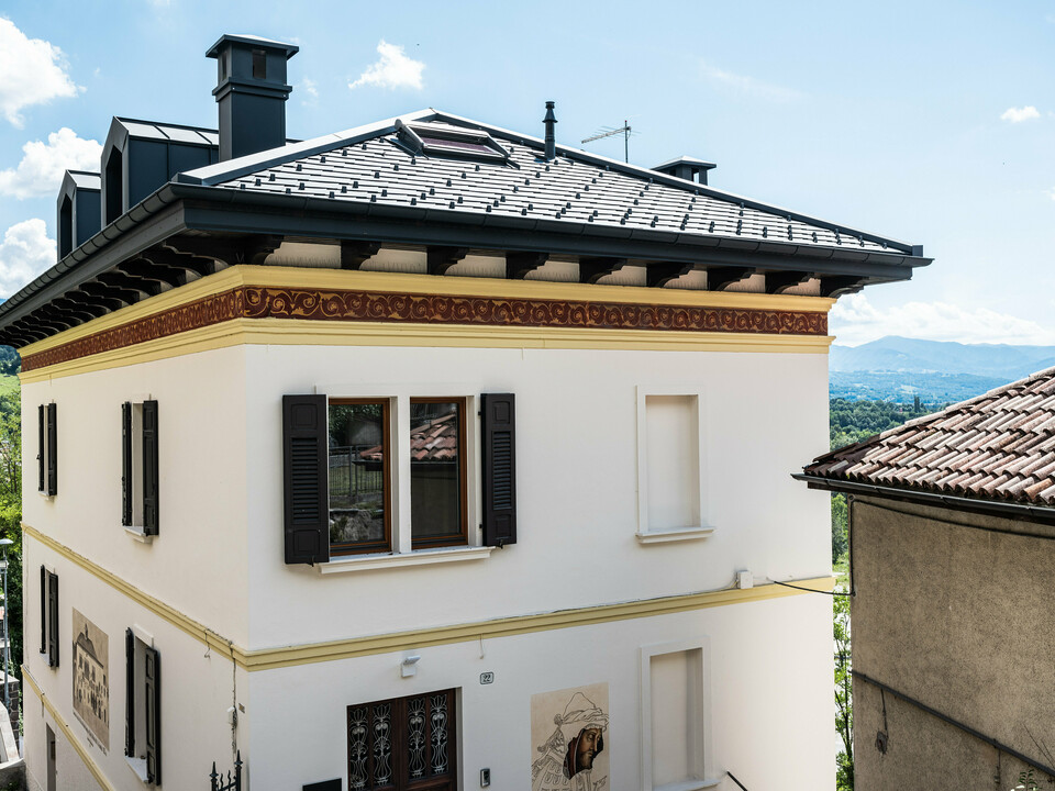 Restauriertes Gebäude in Belluno, gekennzeichnet durch ein PREFA Dach mit anthrazitfarbenen Aluminiumschindeln, die die strukturelle Integrität wahren. Die klassische Fassade mit dekorativen Frieselementen fügt sich nahtlos in die malerische italienische Landschaft ein und wird durch das moderne, langlebige und stilvolle PREFA Dachsystem in der Farbe P.10 Anthrazit abgerundet.