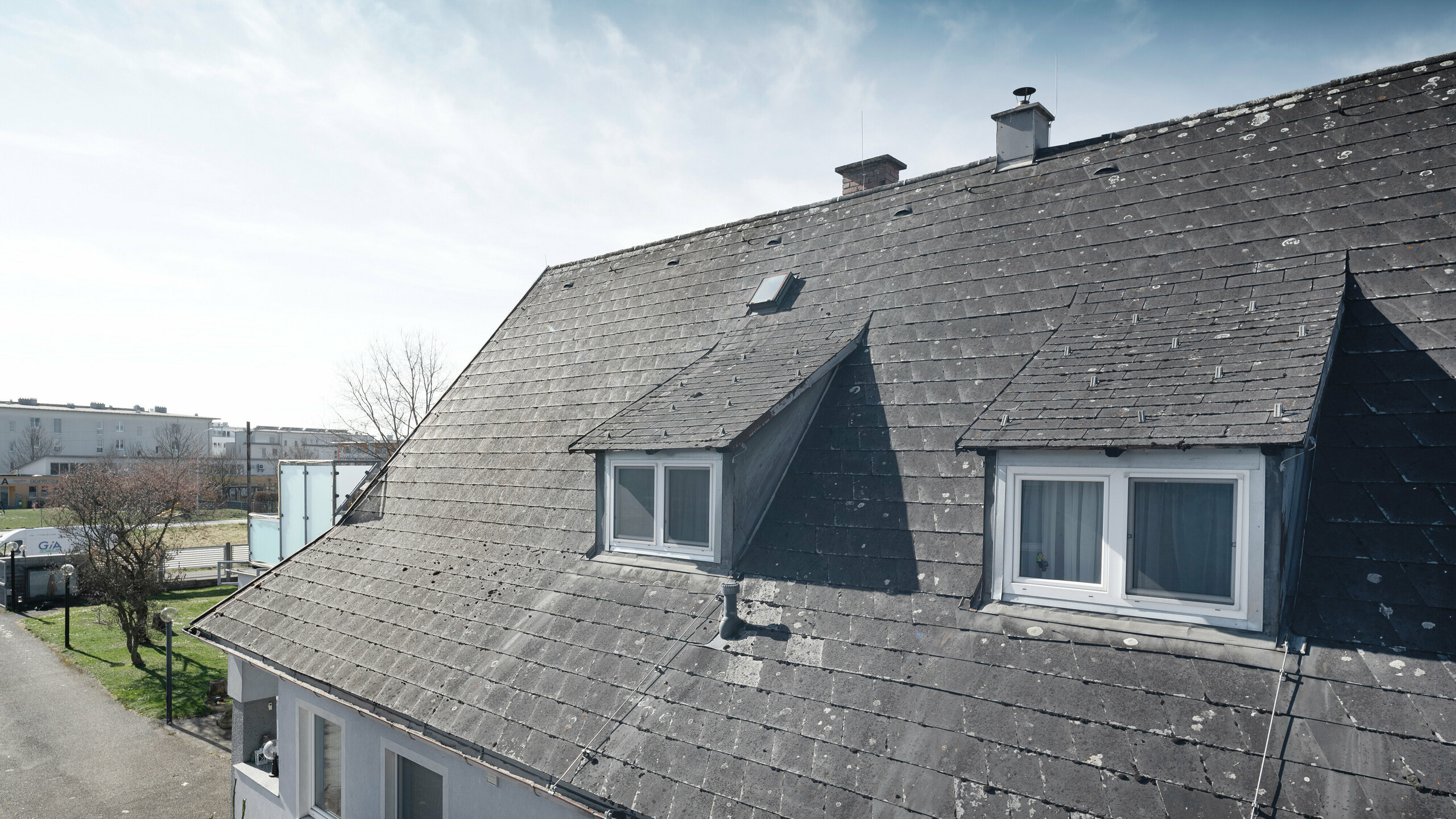 Ein Einfamilienhaus in Leonding (Österreich) wurde vollständig saniert mit PREFA Aluminiumprodukten. Das Bild zeigt das stark verwitterte und abgenutzte Dach von Eternit aus einer seitlichen Perspektive. Die sichtbaren Schäden und Abnutzungen machen die Notwendigkeit einer Dachsanierung und die Installation einer modernen, nachhaltigen Solaranlage deutlich. Diese Aufnahme verdeutlicht den Ausgangszustand vor der Transformation.