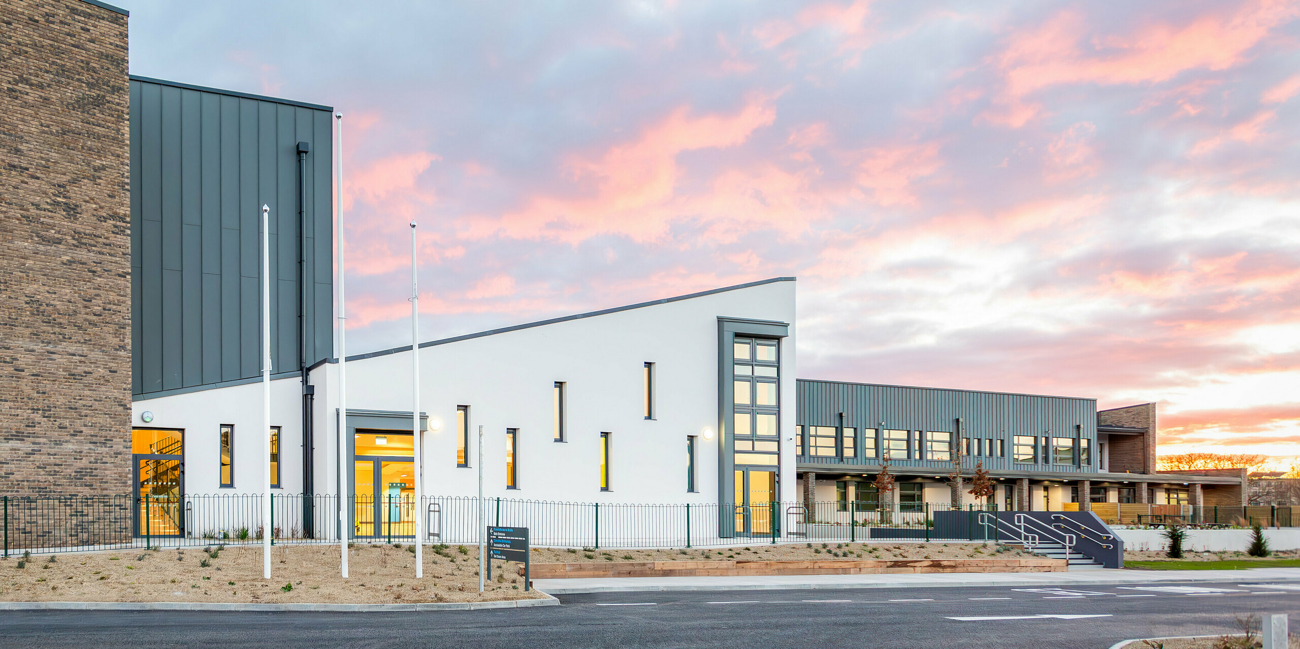 Das moderne Schulgebäude der Scoil Mhuire Naofa in Carrigtwohill, Irland, präsentiert sich mit einer markanten Aluminium-Fassade aus PREFALZ in P.10 Hellgrau. Die langlebige und witterungsbeständige Stehfalzdeckung umfasst rund 800 m² und verbindet Funktionalität mit zeitloser Ästhetik. Vor der Kulisse eines malerischen Sonnenuntergangs kommt die hochwertige Architektur besonders gut zur Geltung.